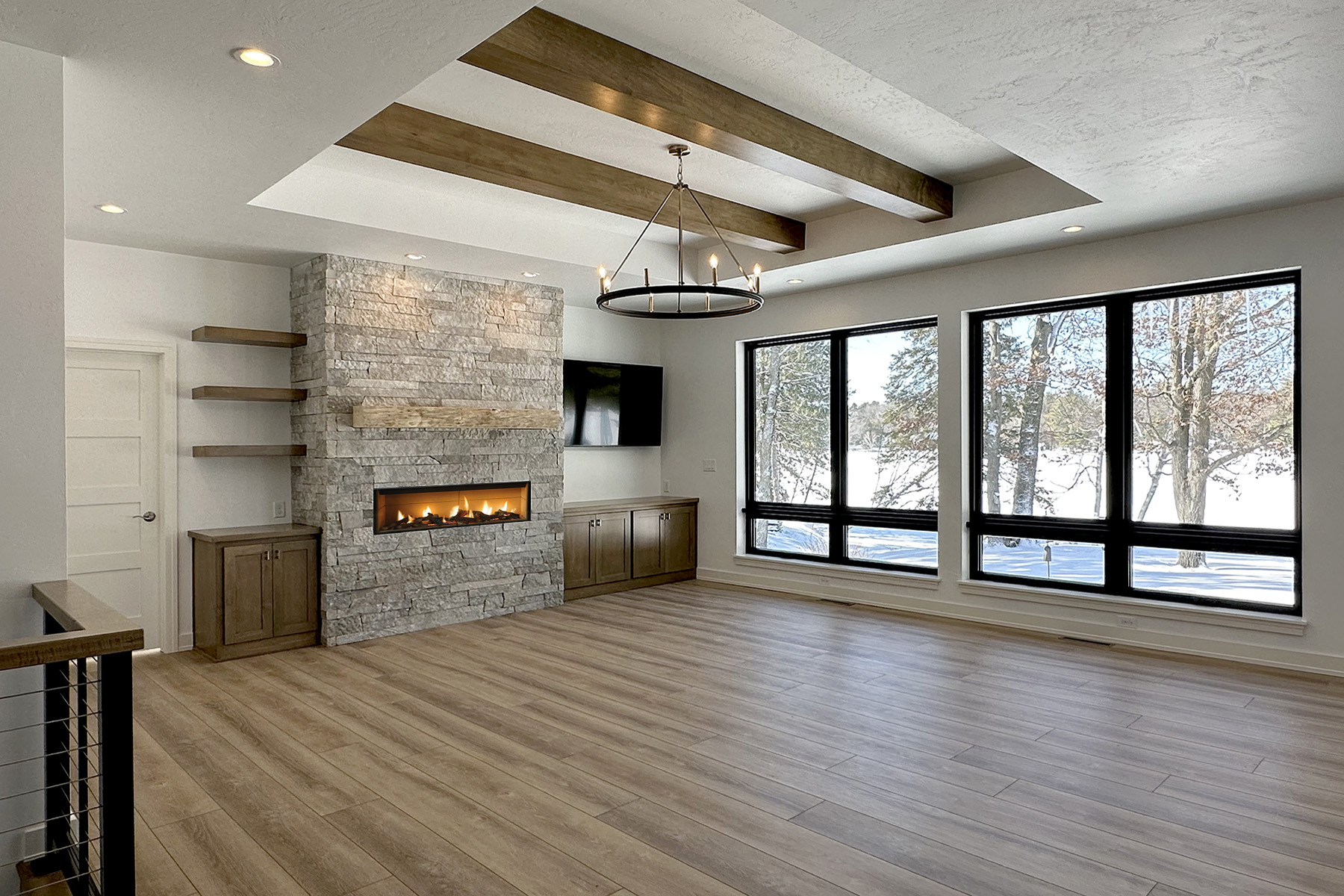 N3101 Right of Way Road Great Room. Stacked Stone Linear Modern Fireplace. Built-in Cabinets with Floating Shelves. Black windows with plastered drywall returns. Tray ceiling with stained maple wood beams. Luxury vinyl plank floors. 4-panel interior doors.