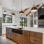 704 Royal St Pats Kitchen Living Room Fireplace Ceiling Beams1 704 Royal St Pats Kitchen. Painted Perimeter Cabinets with Stained Maple Island and Custom Wood Hood. Pendant Lights. Under-Counter Beverage Center Refrigerator. Interior Transom. White Vertical Picket Tiled Backsplash. Glass Doors Above Upper Cabinets. Calacatta Prado Quartz with Black Pearl Brushed Granite Countertops. Black Painted Shiplap (Sherwin-Williams Iron Ore SW-7069) Fireplace Surround with Mitered Corners and Reclaimed Hewn Timber Mantel. Stained Maple Floating Shelves. TV Above Fireplace. Luxury Vinyl Plank Flooring. Hewn Timber Ceiling Beams at Vaulted Ceiling. Black Windows with White Painted Trim.
