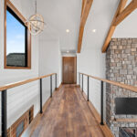 10510 Sugar Creek Balcony. Black cable railing with maple handrail. Vinyl plank flooring. 2-story great room with ceiling beams and stone fireplace. Balcony catwalk.