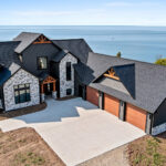 10510 Sugar Creek Exterior. Black siding with black windows. Decorative gable beams. Woodgrain overhead garage doors.