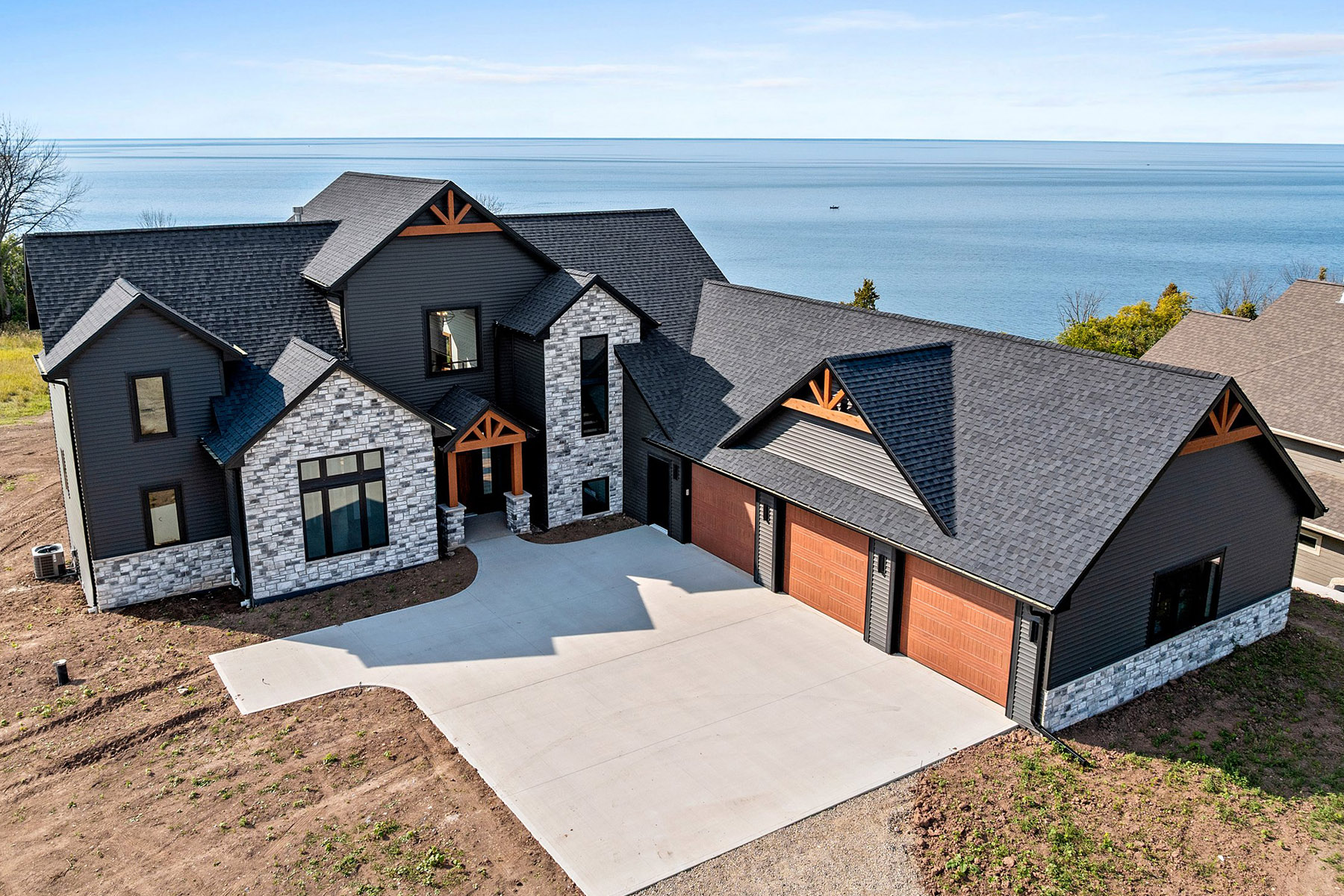 10510 Sugar Creek Exterior. Black siding with black windows. Decorative gable beams. Woodgrain overhead garage doors.