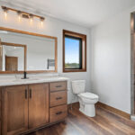 10510 Sugar Creek Full Bathroom. Maple vanity cabinet with stone countertops, walk-in tiled shower, wood-framed mirror, vinyl plank floors.