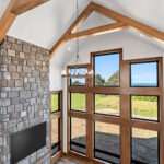 10510 Sugar Creek Great Room + Fireplace. Black interior windows, 2-story great room window wall, vinyl plank floors, ceiling beams, stone fireplace surround with lightweight concrete mantel.