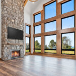 10510 Sugar Creek Great Room + Fireplace. Black interior windows, 2-story great room window wall, vinyl plank floors, ceiling beams, stone fireplace surround with lightweight concrete mantel.