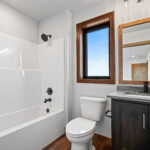 10510 Sugar Creek Guest Bathroom. Maple vanity cabinet with stone countertops, wood-framed mirror, vinyl plank floors.