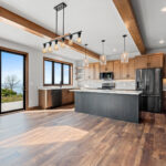 10510 Sugar Creek Kitchen & Dining. Custom maple cabinets, black island, quartz countertops, vinyl plank floors, ceiling beams, floating shelves, black interior windows over kitchen sink, under-cabinet lighting, tiled backsplash.