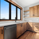10510 Sugar Creek Kitchen. Custom maple cabinets, quartz countertops, vinyl plank floors, floating shelves, black interior windows over kitchen sink, under-cabinet lighting, tiled backsplash.