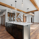 10510 Sugar Creek Kitchen. Custom maple cabinets, quartz countertops, vinyl plank floors, stone fireplace, ceiling beams, open riser glu-lam stairs with black cable rail.