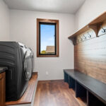 10510 Sugar Creek Laundry & Mud Room. Maple Bench with Board, Coat Hooks, Shelf & Shiplap. Vinyl plank flooring. Black interior window. Built-In raised laundry pedestal.