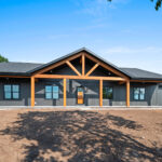9185 Rasner Exterior. Covered Porch Cedar Timber Post & Beam. Black Vertical Board & Batten Siding Gentek Iron Ore. Black Windows.