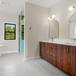 9185 Rasner Owners Bathroom. Vertican Grain Black Walnut Slab Front Modern Vanity Cabinet with Calacatta Sonata White Granite Countertops & Champagne Bronze Hardware & Fixtures. Angora Station Invory Half Hexagon Tiled Flooring. Walk-In Tiled Shower. Freestanding Tub.