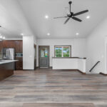 4673 Mill Rd Great Room + Foyer. Lone Star Spirit "Ballroom Rodeo" 9" Wide Vinyl Plank Flooring. Cathedral Ceiling. Stained Maple Cabinetry + Woodwork. Half Wall with Maple Cap Stairwell.