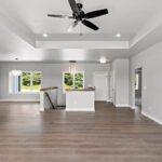 E1999 Hillside Great Room. Kentmore Lodge "Natural Canvas Oak" Vinyl Plank Flooring. Stairs with Half Wall and Wood Cap. Tray Ceiling. Open Concept. Dining to Front of House.