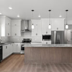 E1999 Hillside Kitchen. Kentmore Lodge "Natural Canvas Oak" Vinyl Plank Flooring. White Painted Cabinets to 9'-0" Ceiling Height. Chimney Range Hood. Built-In Microwave. River Blue Leathered Granite Countertops. Center Island.